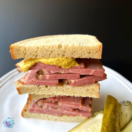 Pastrami sandwiches on a white plate with pickles.