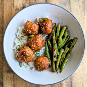 White plate with rice topped with Slow Cooker Spicy Korean Meatballs with green beans on the side.