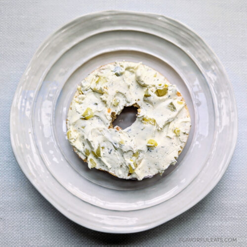 Dill Pickle Cream Cheese Spread on a bagel on a white plate